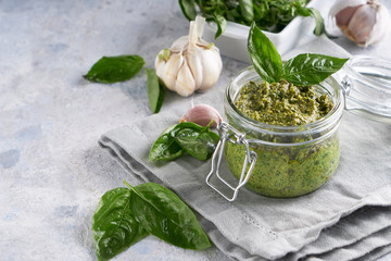 traditional italian basil pesto sauce in a glass jar on a light stone table Copy space