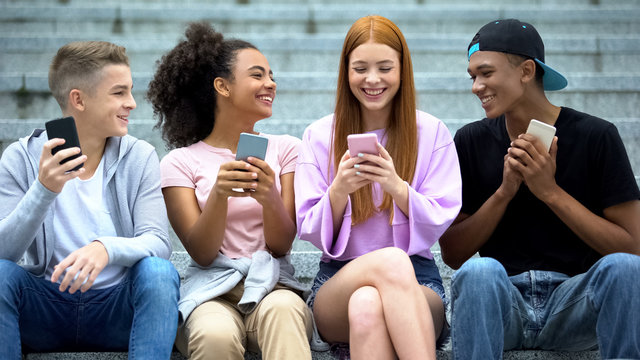 Joyful friends smartphones sitting campus stairs together, digital generation