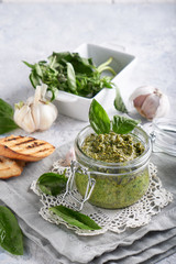 traditional italian basil pesto sauce in a glass jar wiht toasts on a light stone table
