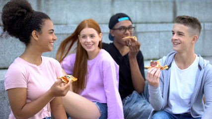 Obraz premium Young multiethnic friends laughing enjoying pizza, adolescence positivity, fun