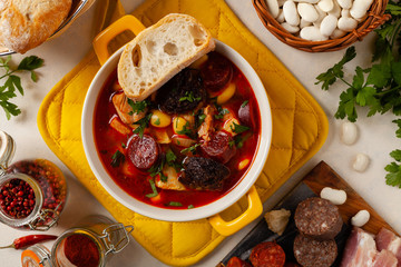 Traditional Spanish goulash soup. Fabada Asturiana. Served with a yellow clay pot with lid. Top view.