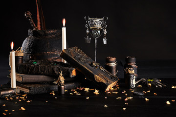 Books with spells, old pot, jars of potion are on a wooden dark table. Petals of dried roses are...