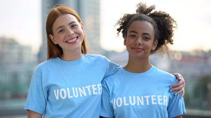 Two female volunteers smiling on camera, high school charity program, altruism