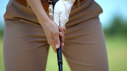 Female in white glove with golf club studying to play basic ball position, sport