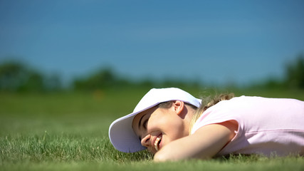 Funny young girl golfer rejoicing successful shot, lying on course near hole