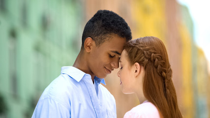 Multiethnic teen couple touching foreheads looking into eyes with love, romance