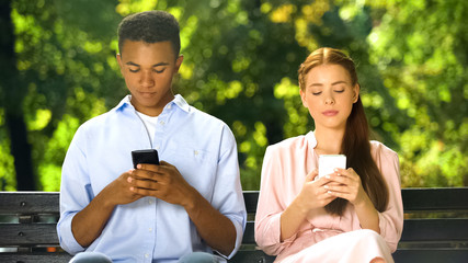 Mixed-race boy making compliment to gadget-addicted girl in social network, fail