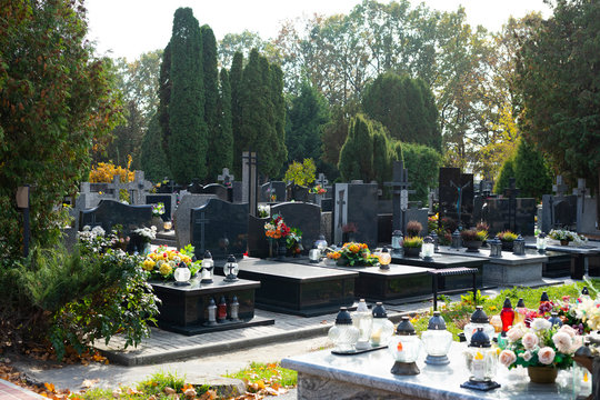Graves at a Christian cemetery in autumn. All Saints Day. Tombstones decorated with flowers and grave candles.