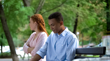 Fototapeta premium Offended teen girlfriend and boyfriend sitting separately on bench in park