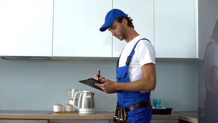 Man with tools writing report inspecting kitchen on electrical safety, service