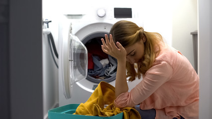 Tired woman loading clothes in washing machine, annoyed with housework routine