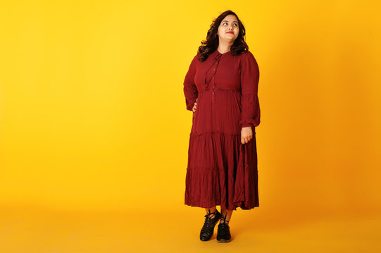 Attractive South Asian Woman In Deep Red Gown Dress Posed At Studio On Yellow Background.