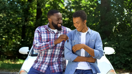Happy dad giving car key to son, permission to drive, parenthood trust, family - 297816977