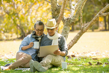  Asian Senior couple sitting at park while using laptop
