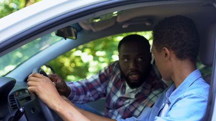 Male instructor teaching teen how to drive car, automobile school, license exam