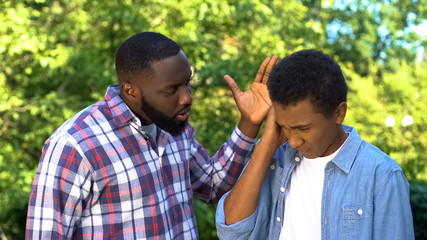 Angry male hitting son upside head shouting outdoors, parenting difficulties