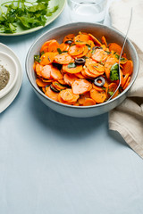 Traditional Moroccan cooked carrot salad North African vegan dish with chopped parsley and olives on gray plate close-up copy space.Healthy organic food for holiday dinner.Vertical orientation