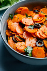 Traditional Moroccan cooked carrot salad North African vegan dish with chopped parsley and olives on gray plate close-up.Healthy organic food for holiday dinner.Vertical orientation