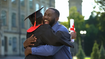 Cheerful father and graduating son hugging outdoor, study achievement, education - 297817773