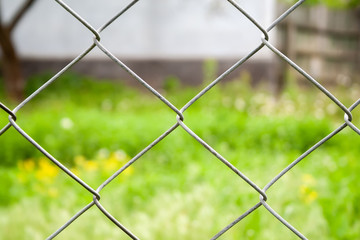 Blurred countryside view through a metal fence on green grass and a house