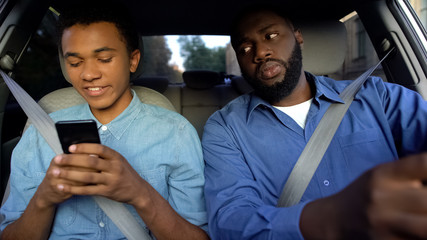 Joyful afro-american teen texting phone dad trying to read message while driving
