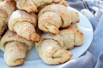 Closeup view of ruddy sugar-frosted croissants from a curd dough lying on a white plate next to a gray cloth. Sweet baked bagels just taken out of the oven. A delicious tea snack for breakfast