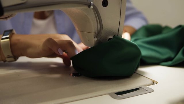 Closeup of a young woman's hands with manucure sewing green fabric with a sewing machine. Women's hands sew on a sewing machine. Fashion, creation and tailoring