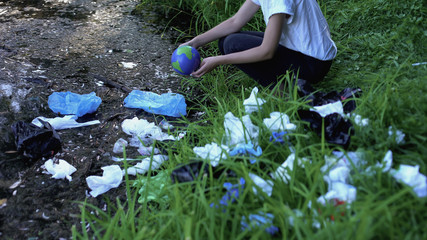 Woman taking Earth globe from polluted lake in forest, waste recycling problem