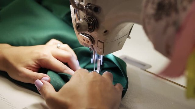 Closeup of a young woman's hands with manucure sewing green fabric with a sewing machine. Women's hands sew on a sewing machine. Fashion, creation and tailoring. High angle view
