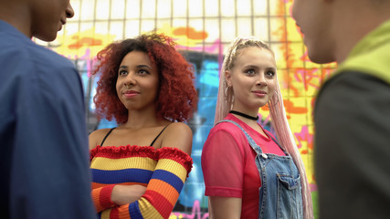 Fashionable female friends looking at male teenagers, young people flirting