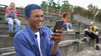 Happy male teen laughing reading smartphone joke, digital generation, internet