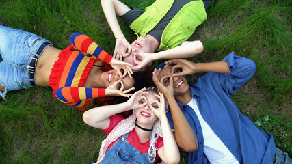 Happy young people showing ok gesture like binoculars lying campus park grass