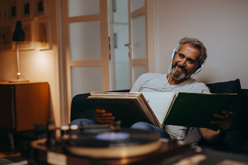 man listening music on headphones in his home. choosing records - obrazy, fototapety, plakaty