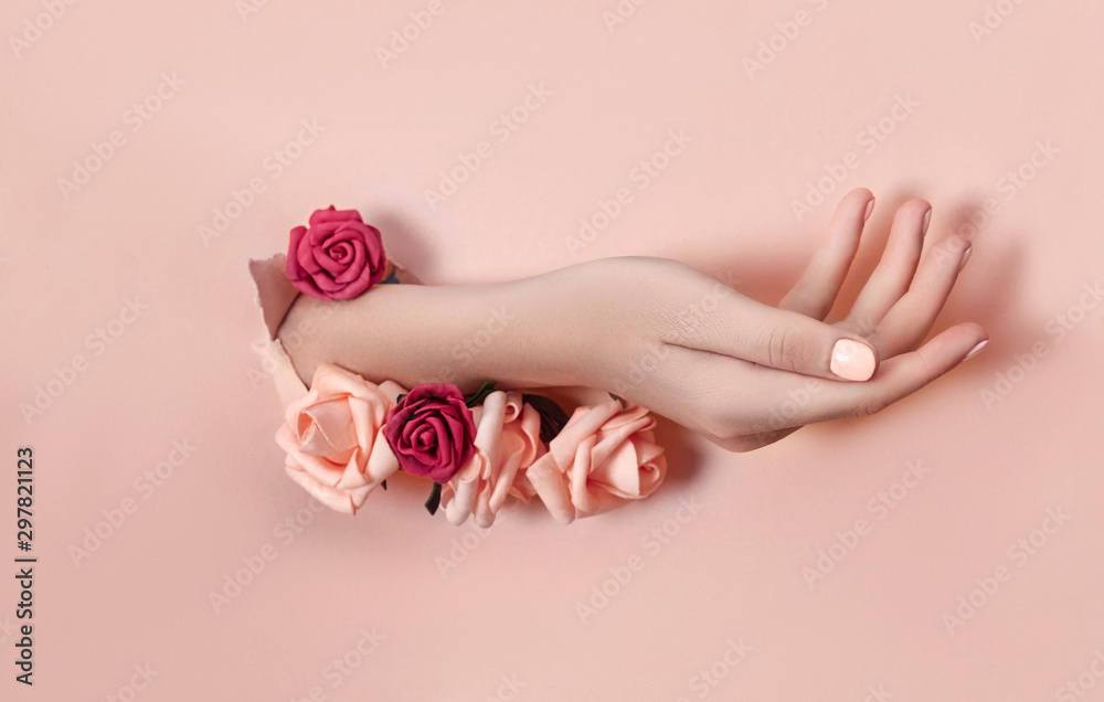 Wall mural Hand with paper flowers and painted nails is thrust through a hole in the paper background. Cosmetics and hand care, moisturizing and wrinkle reduction