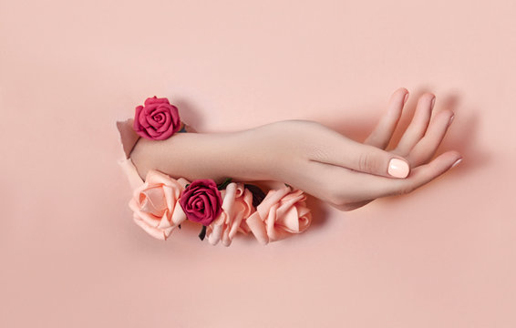 Hand With Paper Flowers And Painted Nails Is Thrust Through A Hole In The Paper Background. Cosmetics And Hand Care, Moisturizing And Wrinkle Reduction