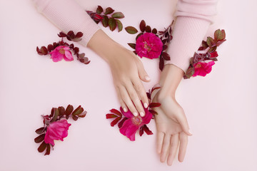 Obraz na płótnie Canvas Beauty Hand of a woman with red flowers lies on table, pink paper background. Natural cosmetics product and hand care, moisturizing and wrinkle reduction, skincare