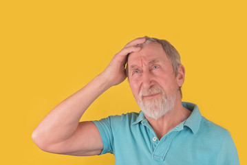 Elder man with beard and grey hair thinking, holding one hand on head  over yellow background