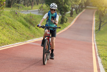 Obraz na płótnie Canvas Riding on park bike path,using smartphone while riding bike on sunny day