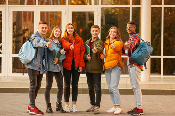 Group of teenage students showing thumb-up near university