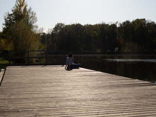 Woman sitting on wooden pier on river bank on sunny day with trees surrounding river