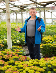 Positive man florist looking for plant of  hortensia in pots while gardening