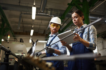 Female foreman in work wear using digital tablet and controlling the work while man working with...