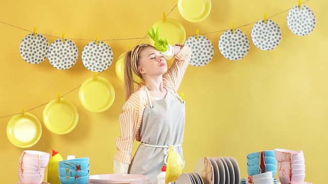 Beautiful blonde woman with hand on her forehead and closed eyes standing behind the table full of unwashed dishes. Spare time. Difficult housework