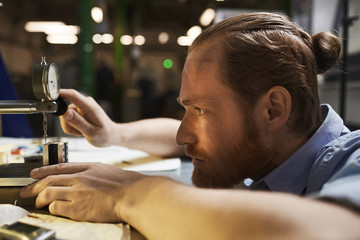 Close-up of serious technician working on lathe he controlling the quality of products in the factory