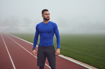 A male athlete in training stands at the stadium in the fog.