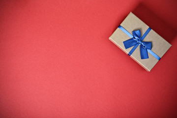 Christmas and New Year composition. Gift box with a blue bow on red background. Christmas, birthday, anniversary, new year, Valentine's day, Father's day concept. Flat lay, top view, copy space.