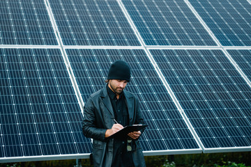 Man make notes into clipboard beside of solar panels