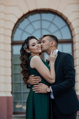 Stunning young couple. Family photo, romantic couple. Best time. Young man in suit embrase and kiss young wonderful woman in green dress. Loving couple enjoying in moments