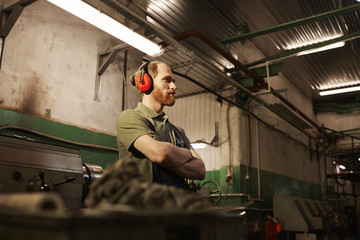 Young bearded man in work wear standing with arms crossed he working in the plant