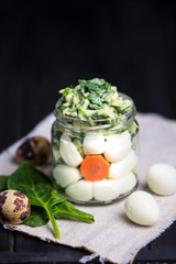 salad with spinach, quail egg and sauce in a glass jar on a dark background